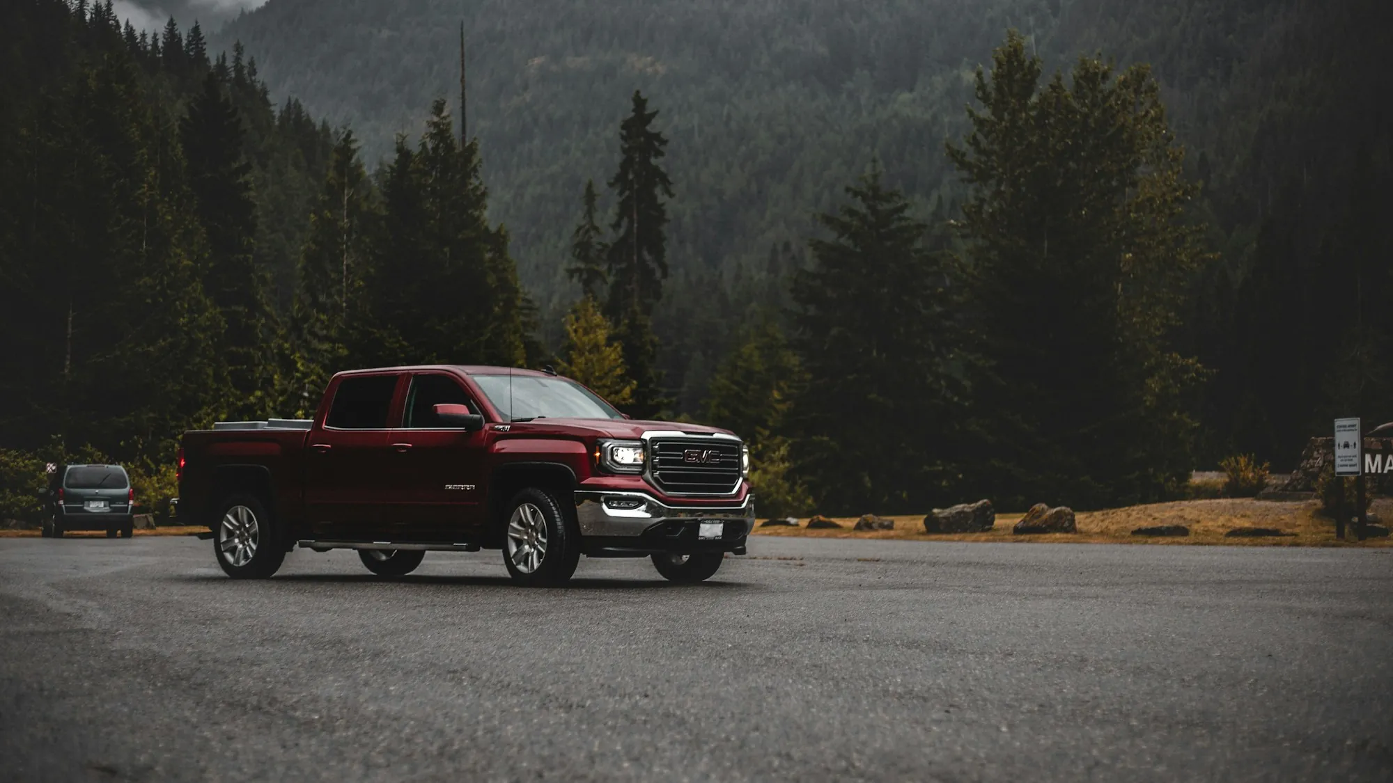 Black pickup truck on a gravel road in front of forested mountains