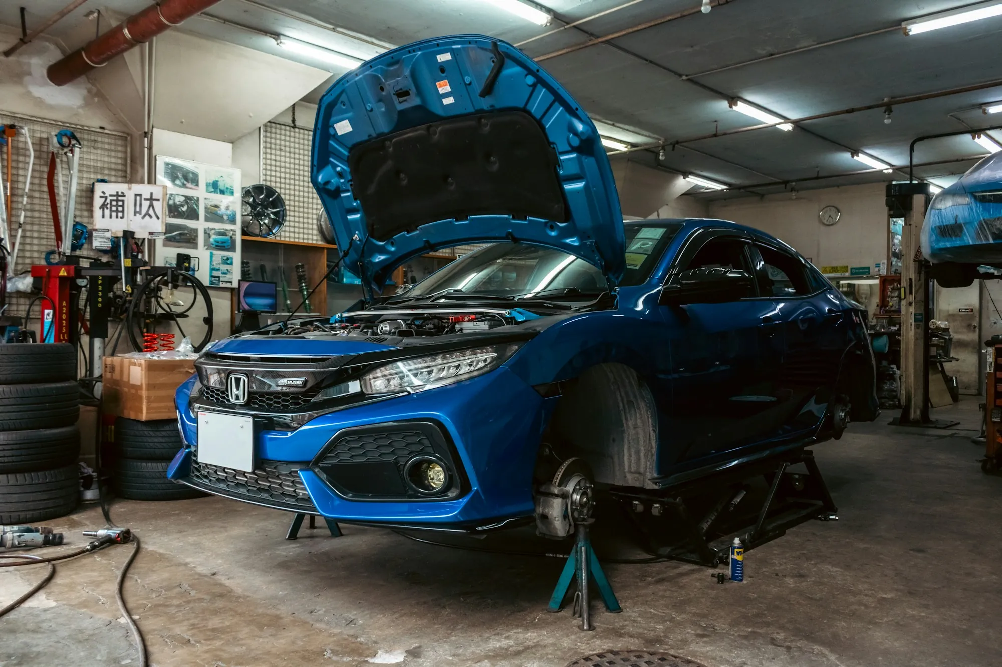 Mechanic working on a blue hatchback raised on a lift with its hood open